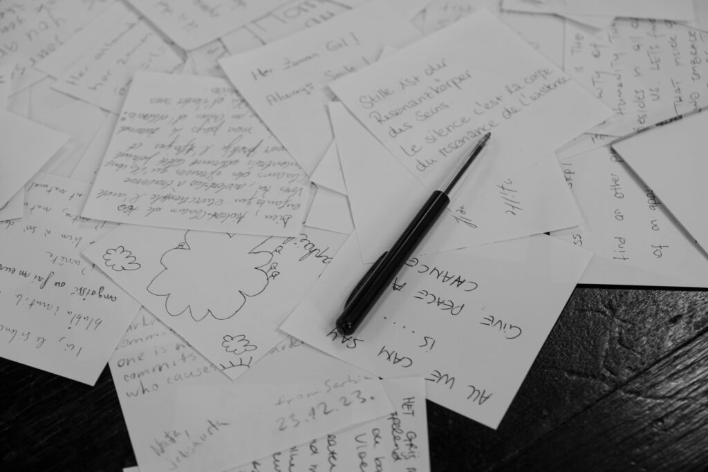 A collection of handwritten notes scattered on a desk with a pen in black and white.