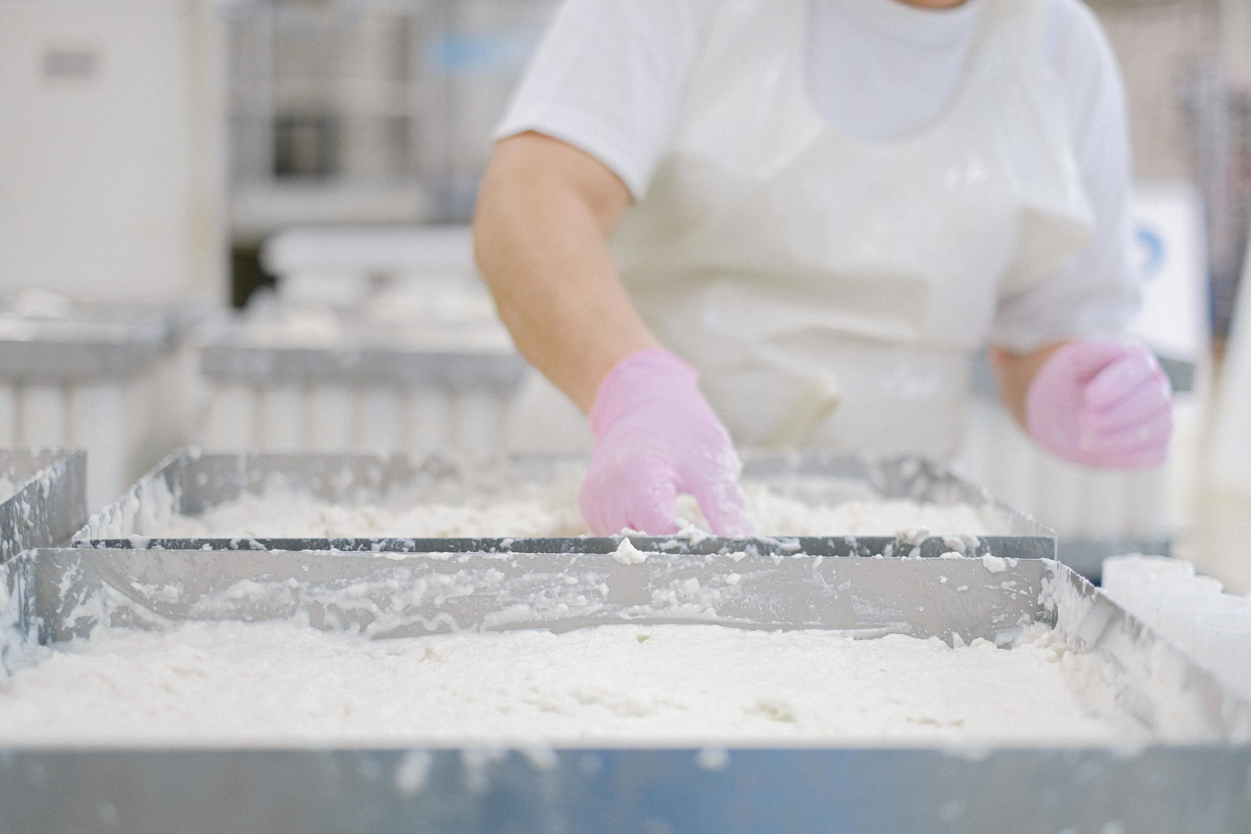 Close-up of a worker processing dairy products wearing gloves and an apron.
